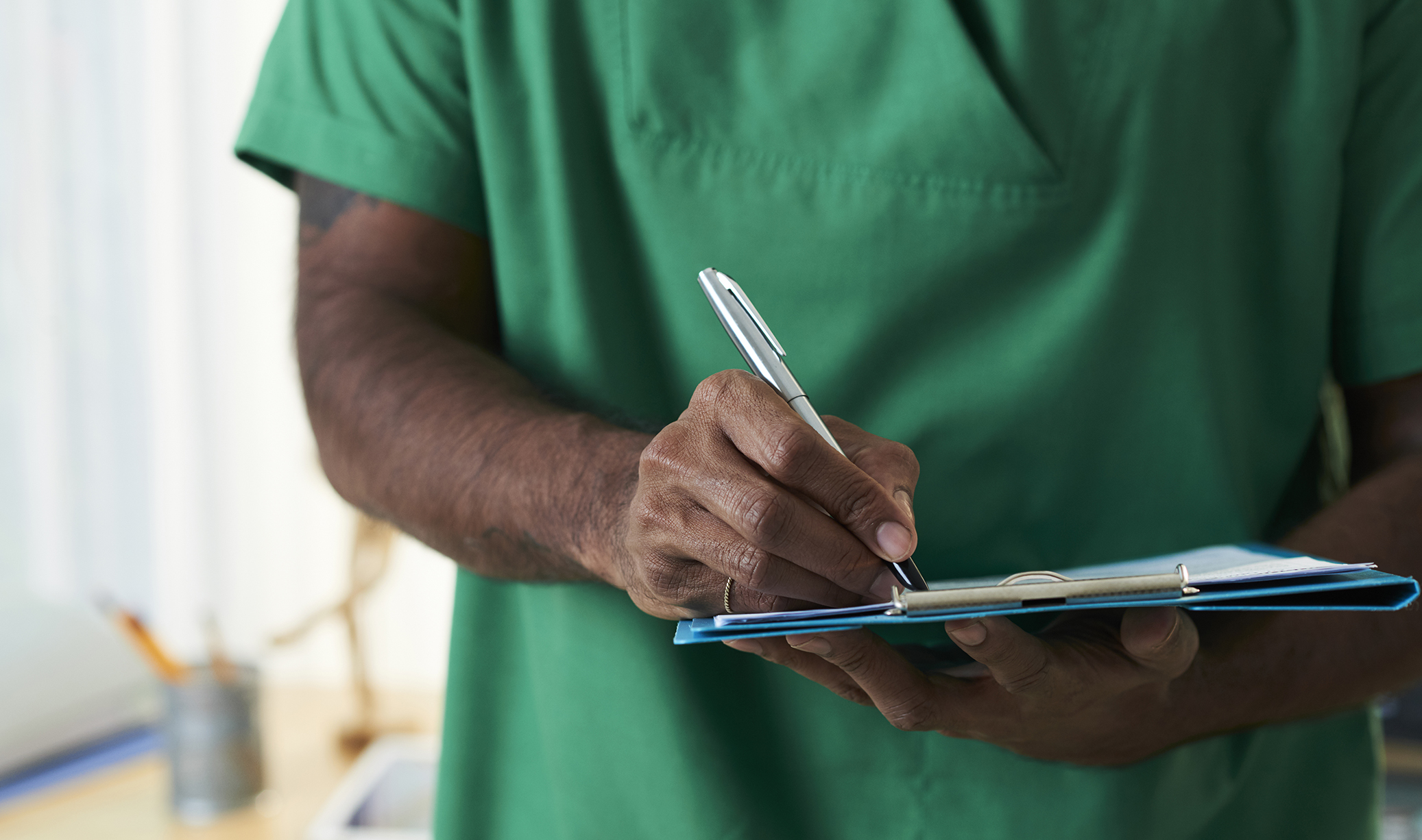 Hand of mixed-race doctor writing down prescriptions or diagnosis on paper while working in clinics